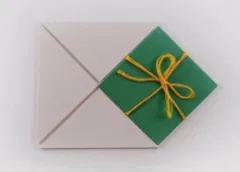 Green gift box with gold ribbon beside gray envelope on white surface