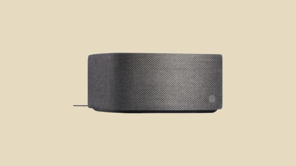 Front view of a rectangular dark grey Bluetooth speaker with rounded edges and small circular logo, on a cream background.