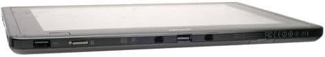 Side view of a black tablet showing USB port, headphone jack, and volume buttons; device rests on a white surface.