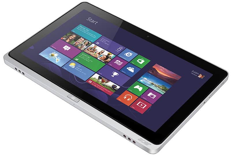Tablet showing Windows 8 start screen with colorful tiles, lying flat on white surface, viewed from a front-side angle.
