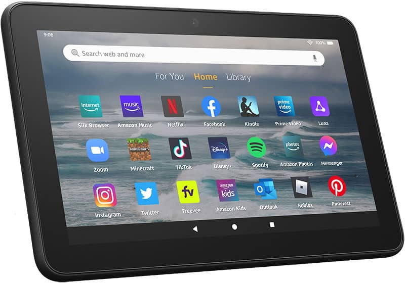 Front view of a black Amazon Fire tablet showing home screen with popular apps, cloudy beach wallpaper in background.