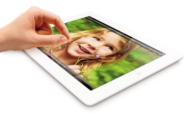 Front view of a hand using a white Apple iPad, displaying a smiling child with green plants in the background.