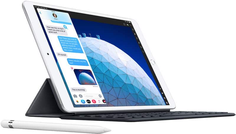 Front angled view of tablet with keyboard case, messaging app open, geometric blue wallpaper, white stylus in front. Brand/model unclear.