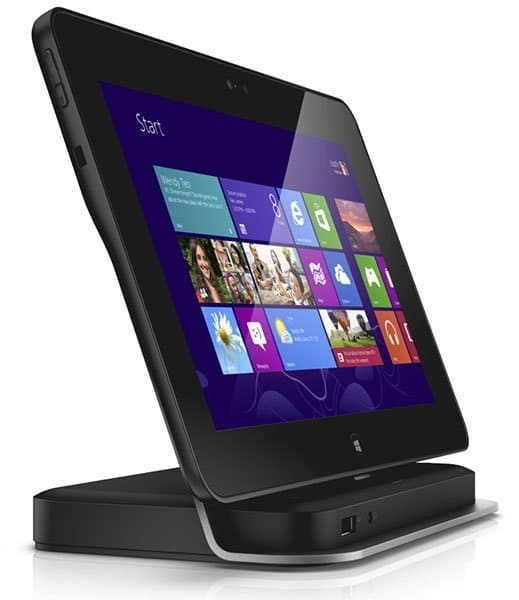 Angled front view of a black tablet docked on a charging station, displaying the Windows 8 Start screen on a white background.
