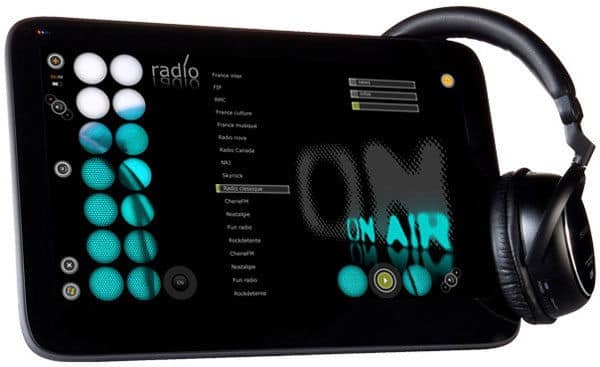 Front view of a tablet showing a radio streaming app, with black over-ear headphones resting on the device’s edge.