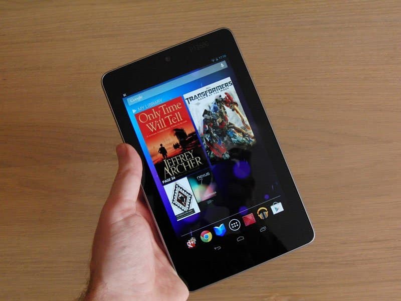 Front view of a hand holding a black tablet, likely Amazon Fire, showing eBooks and a "Transformers" movie poster on screen.