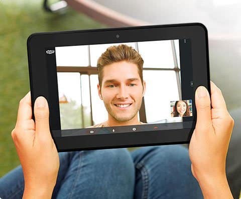 Front view of user holding Samsung Galaxy Tab on a video call, main screen shows man smiling, small window with woman.