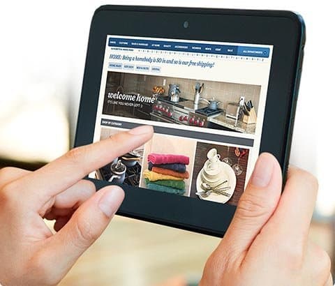 Front view of a person tapping a Samsung Galaxy Tab, browsing home goods, cookware, and towels online.