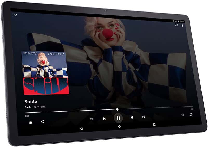 Front view of a tablet, music player app open with "Smile" by Katy Perry album art and controls; background shows a woman in clown nose.