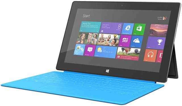 Front view of Microsoft Surface with blue keyboard, Windows 8 Start screen, colorful tiles, and kickstand extended.