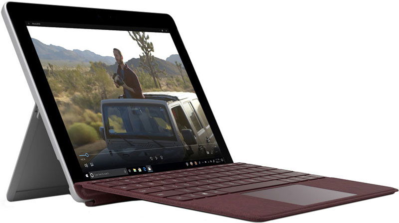 Front view of a tablet with maroon keyboard cover on kickstand, showing a video of someone standing through a car sunroof in the desert.