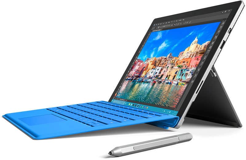 Front view of a tablet with blue keyboard and silver stylus on white, screen displaying colorful seaside town scene.