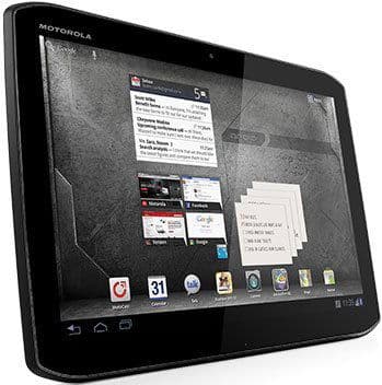 Front view of a Motorola tablet, screen angled slightly right, showing home screen with app icons and widgets on gray background.