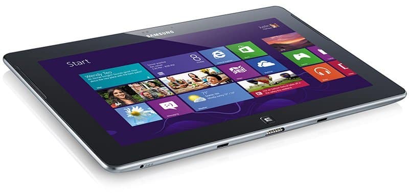 Samsung tablet (likely ATIV model) front view at slight angle, Windows 8 start screen with colorful tiles on purple background.