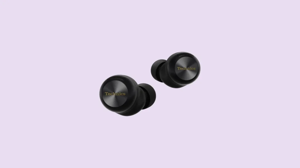 Front view of black Technics wireless earbuds with gold logos, shown on a light purple background.