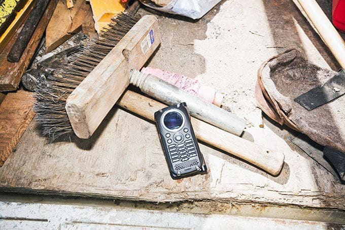 Casio Brigade G'zOne phone displayed front-facing on a dusty work surface surrounded by tools and construction materials