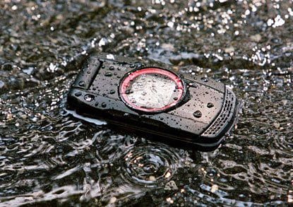 Casio GzOne Ravine submerged in water, front view, showing rugged black casing with red circular dial and water droplets covering the surface