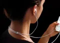 White earbud-style headphones worn in ear with cord visible against black background