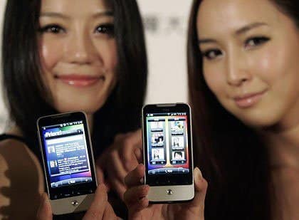 Two people holding HTC Legend phones, displaying the front screens with apps and interface visible