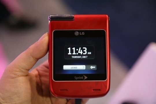 Front view of red LG Lotus Elite flip phone in hand; external screen shows time, date, and Sprint logo below display.