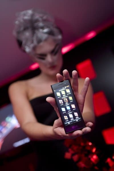 LG New Chocolate phone held up by a woman, displaying its grid of illuminated buttons against a purple and red lit background