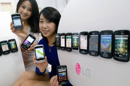 Two women displaying a collection of LG Optimus One smartphones in various colors and models, arranged on a white surface