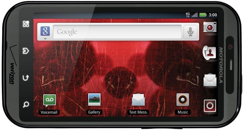 Motorola Droid Bionic front view with red wallpaper, Google search bar, and app icons including Voicemail, Gallery, Text Mess, and Music on screen