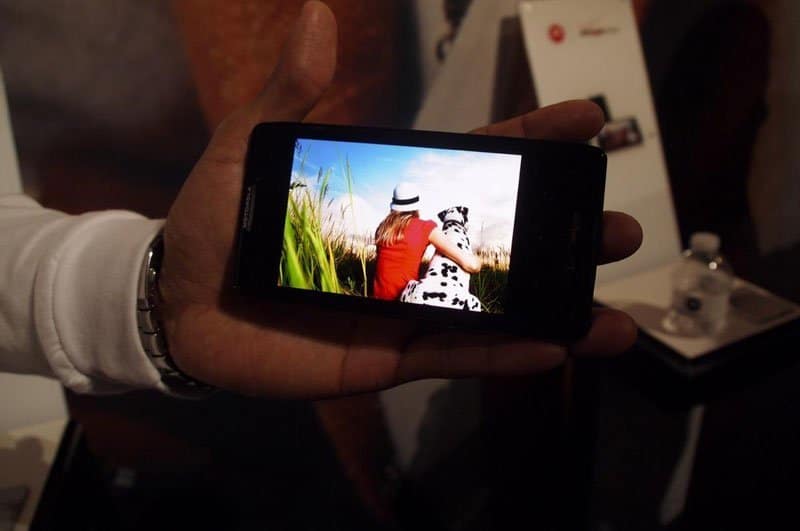 Motorola DROID RAZR MAXX HD held in hand displaying photo of person in red shirt and dog in field on screen