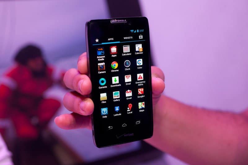 Motorola DROID RAZR MAXX HD held in hand, front view with screen on displaying app grid against purple background