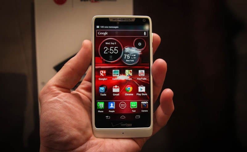 Motorola DROID RAZR M front view with screen on, displaying home screen with clock widget showing 2:55 and app grid, held in a person's hand