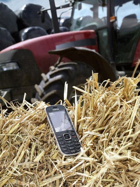 Nokia 3720 Classic phone resting in dried straw with a red tractor blurred in the background