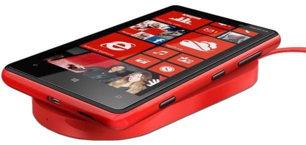 Nokia Lumia 820 in red, front-facing view with screen on, resting on a red wireless charging pad with cable attached