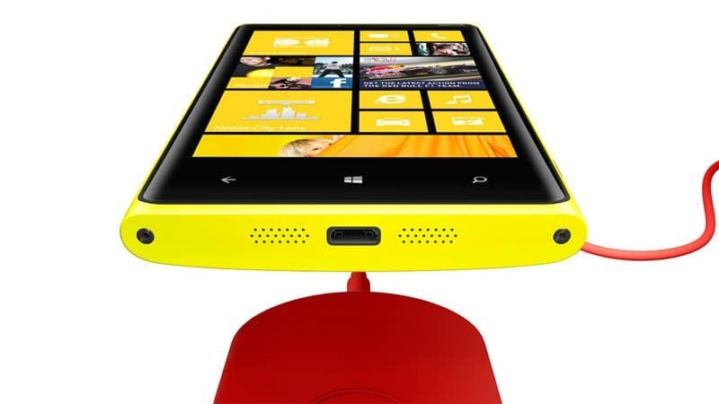 Front view of yellow Nokia Lumia 920 on red circular wireless charging pad, screen showing Windows app tiles.