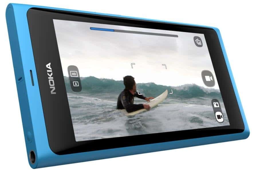 Nokia N9 in cyan blue, front view, displaying photo of person surfing on screen with camera interface visible
