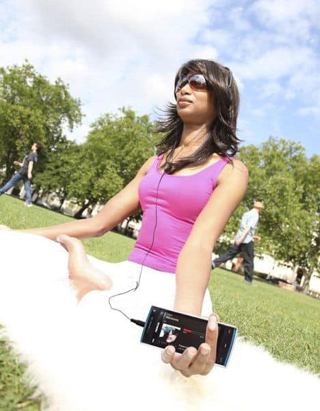 Woman in pink tank top holding Nokia X6 phone with earbuds in a park setting