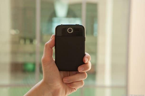 Rear view of a black Pantech Renue smartphone held in hand; blurred indoor background with windows visible.