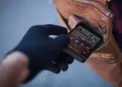 Person in black gloves holding a smartphone against their chest, illustrating phone theft awareness