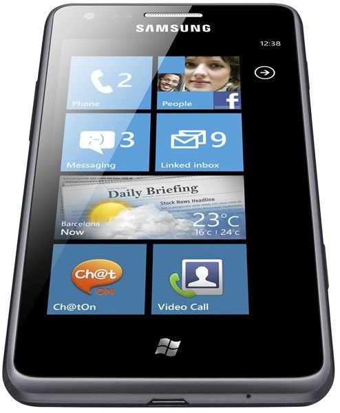 Samsung Omnia M front view with Windows Phone display showing home screen tiles for Phone, People, Messaging, Linked Inbox, Daily Briefing, Chat, and Video Call