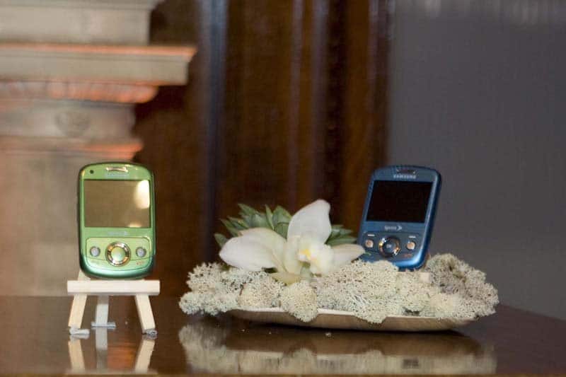 Samsung Reclaim M560 phone in green on left, blue on right, displayed on sand with white flowers and driftwood