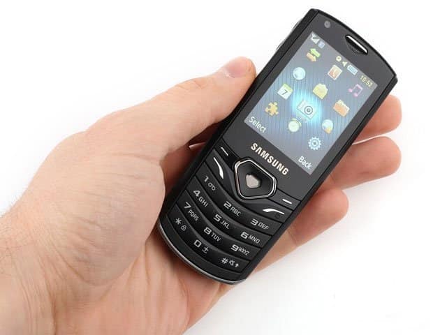 Samsung S5350 Shark phone held in hand, front view with screen on displaying home menu and app icons