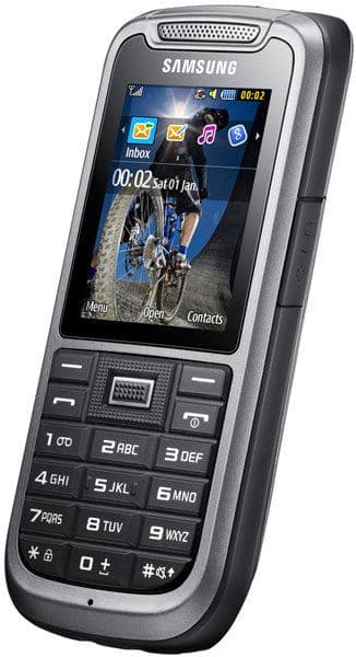 Samsung Solid Xcover front view, rugged flip phone with gray casing, display screen showing time and apps, physical keypad below