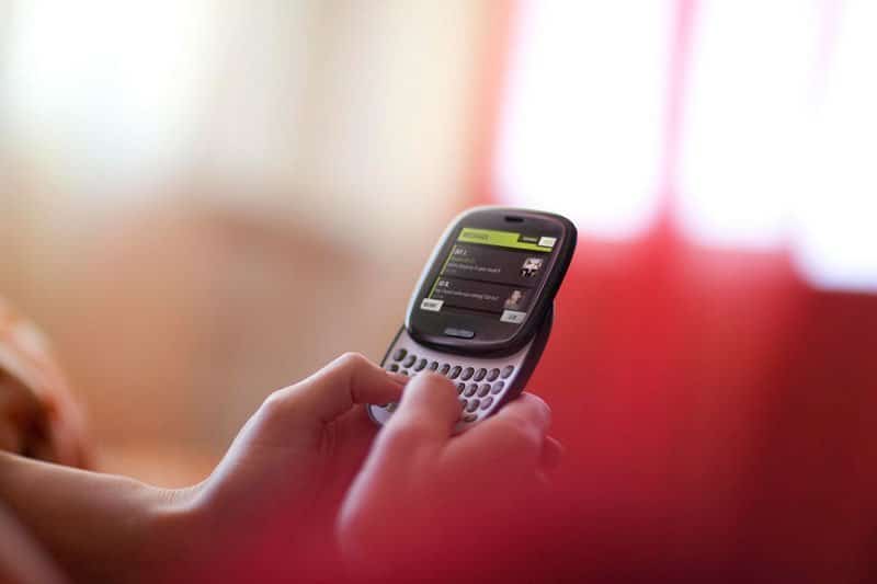 Sharp Kin One smartphone with QWERTY keyboard, held in hand, screen displaying menu interface