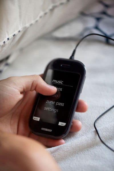 Hand holding Sharp Kin Two phone displaying home screen with music, apps, Zune Pass, and settings options visible