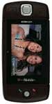 Front view of a closed black Sharp Sidekick LX flip phone with main screen on, displaying a photo of two smiling women.