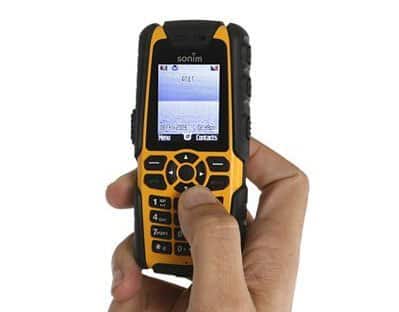 Front view of Sonim XP3 Quest in hand, showing yellow-black rugged design, physical keypad, and menu on small display.