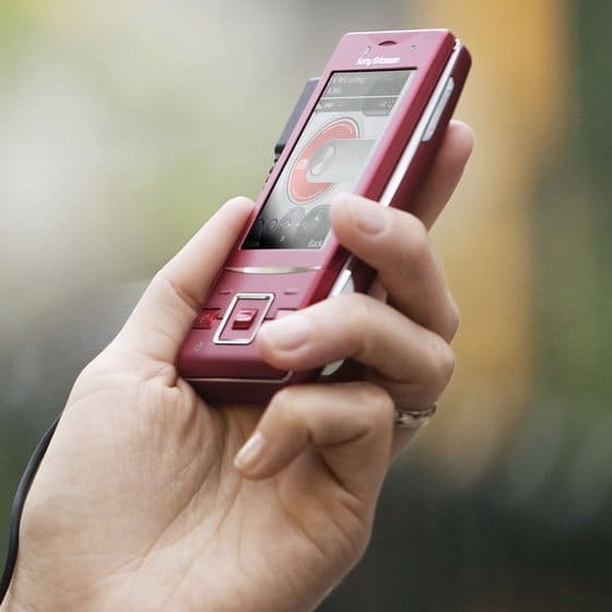 Front view of red Sony Ericsson Hazel held in hand, music player on screen; thumb on keypad, ring visible on finger.