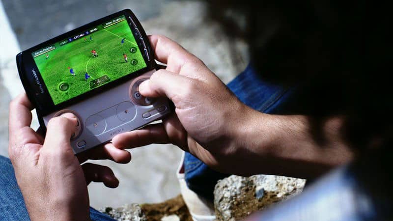 Sony Ericsson Xperia Play held open, displaying a football game on screen with slide-out gamepad controls visible