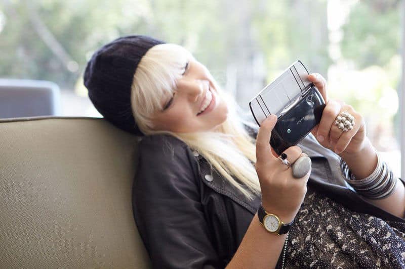 Woman holding Sony Ericsson Xperia Play gaming phone, viewed from front with screen visible, tilted back in relaxed pose