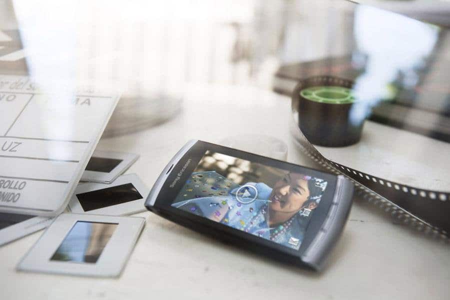 Sony Ericsson Vivaz front view displaying a video on screen, sitting on a desk with papers and a film strip nearby